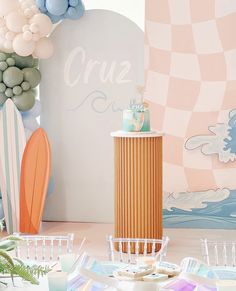 a table topped with plates and cups next to a surfboard wallpaper covered in balloons