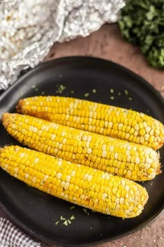 grilled corn on the cob in a black plate next to some silver foil