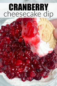 a hand holding a cracker over a cranberry cheesecake dip