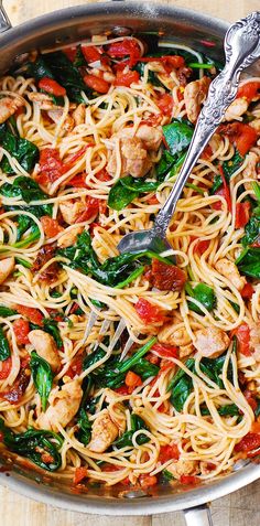 a skillet filled with pasta, chicken and spinach