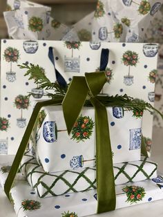 three wrapped presents with green ribbons and bows sit on top of each other in front of wrapping paper