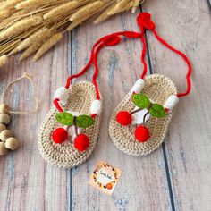 two crocheted slippers with cherries hanging from them on a wooden table