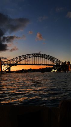 the sydney harbour bridge at sunset as seen from across the water with dark clouds in the sky