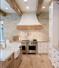 a large kitchen with white cabinets and wood flooring, along with a stainless steel range hood