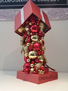 a red and gold christmas ornament on display in a box with the name greaollie