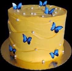 there is a yellow cake with blue butterflies on the top and white pearls around the edges