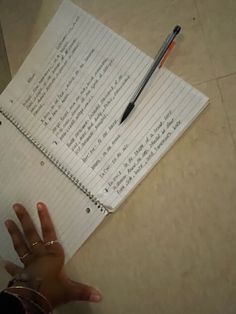 a person holding their hand out in front of a notepad with writing on it