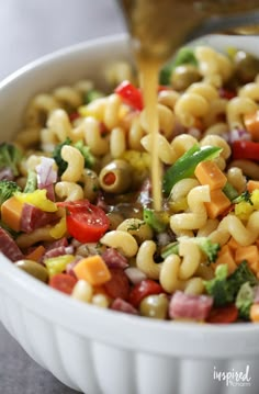 a bowl filled with pasta and vegetables being drizzled on top of it