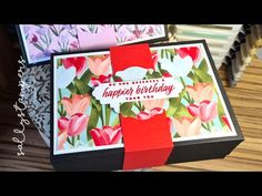 a birthday card in a gift box with a red ribbon on the front and pink flowers on the back