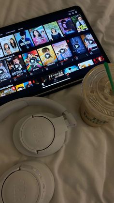 headphones and a drink on a bed next to an electronic device with movies coming out of it