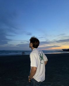 a man standing on top of a sandy beach next to the ocean at sunset or dawn