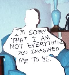 a man sitting in a chair with a sign on his lap reading i'm sorry that i am not everything you imagined me to be