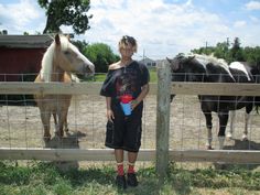 a woman standing next to two horses behind a fence