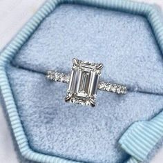 an emerald cut diamond engagement ring in a blue velvet box with ribbon around the band