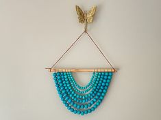 a blue beaded necklace hanging on a wall next to a gold butterfly brooch