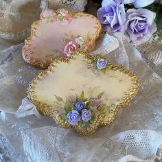 two decorative plates sitting next to each other on a lace covered tablecloth with flowers in the background