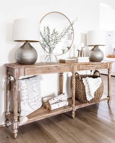 a wooden table topped with two vases filled with flowers next to a wall mounted mirror