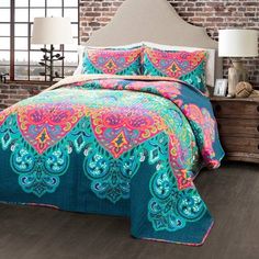 a bed with a colorful comforter and pillows on top of it in front of a brick wall