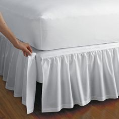 a bed with a white bedspread on top of it and a hand holding the edge of the bed