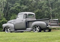 an old gray truck parked on top of a lush green field with trees in the background