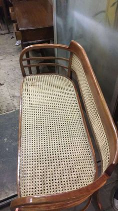 a wooden chair with wicker seat and back rests on the ground in front of a metal door