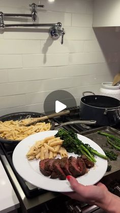 a person is holding a plate with steak and broccoli on it in the kitchen