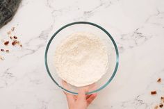 a person holding a bowl filled with flour on top of a white marble countertop