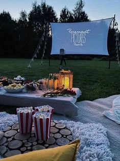 an outdoor movie party with popcorn, sodas and snacks on the grass in front of a screen