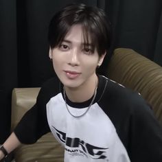 a young man sitting on top of a couch wearing a black and white t - shirt