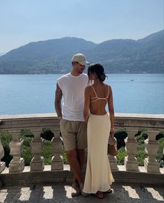 a man and woman standing next to each other in front of a body of water