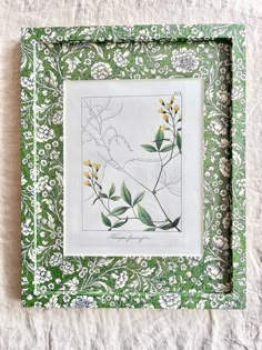 a green and white frame with yellow flowers on the inside is sitting on a bed