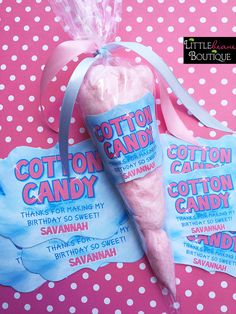 two cotton candy bags are sitting on a pink polka dot tablecloth, one is wrapped in plastic and the other has a blue ribbon