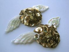 two gold and white brooches with feathers on them sitting next to each other