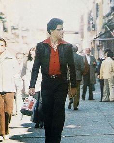 a man is walking down the street with his hand in his pocket and wearing a red shirt