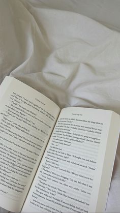 an open book sitting on top of a bed next to a white comforter and pillows