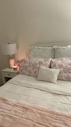 a white bed with pink and white comforter next to a lamp on a nightstand