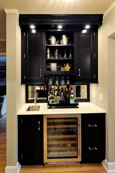 Black built-in home bar with refrigerator, showcase shelves, and cabinets. Wood Cabinetry Kitchen, Cabinetry Kitchen, Glamorous Kitchen, Beige Backsplash