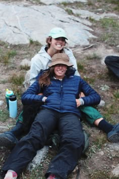 two people are sitting on the ground with their arms around each other and one person is wearing a hat