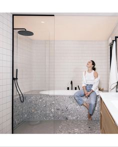 a woman sitting on the edge of a bathtub in a bathroom with white tile walls