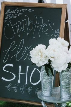 white flowers are in vases next to a chalkboard