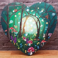 a heart shaped painting on top of a wooden table next to a brick wall with trees and mushrooms painted on it