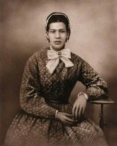 an old black and white photo of a woman sitting on a chair wearing a dress