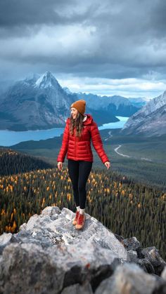 a woman standing on top of a large rock in the middle of a forest with mountains behind her