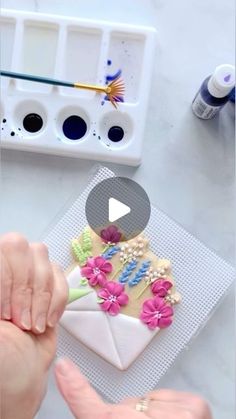 someone is decorating an envelope with flowers and pearls on the outside, while another person holds out their hand