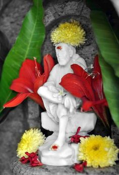 a white statue sitting on top of a rock next to flowers