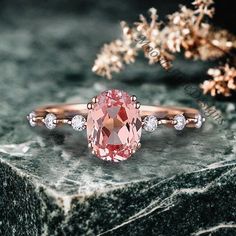 a pink diamond ring sitting on top of a marble table next to some flowers and leaves