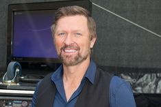 a man with a beard smiles in front of a television