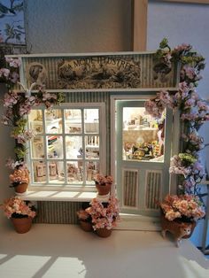 a doll house with flowers on the windowsill and potted plants in front of it