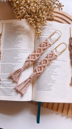 two crocheted tassels are on top of an open book next to some dried flowers