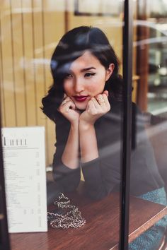 a woman sitting at a table with her hand on her chin looking out the window